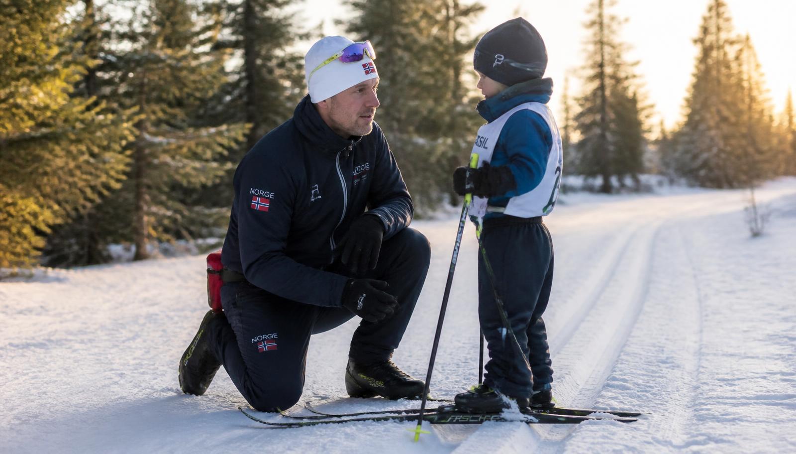 Trener på kne i snøen som snakker med et barn på ski